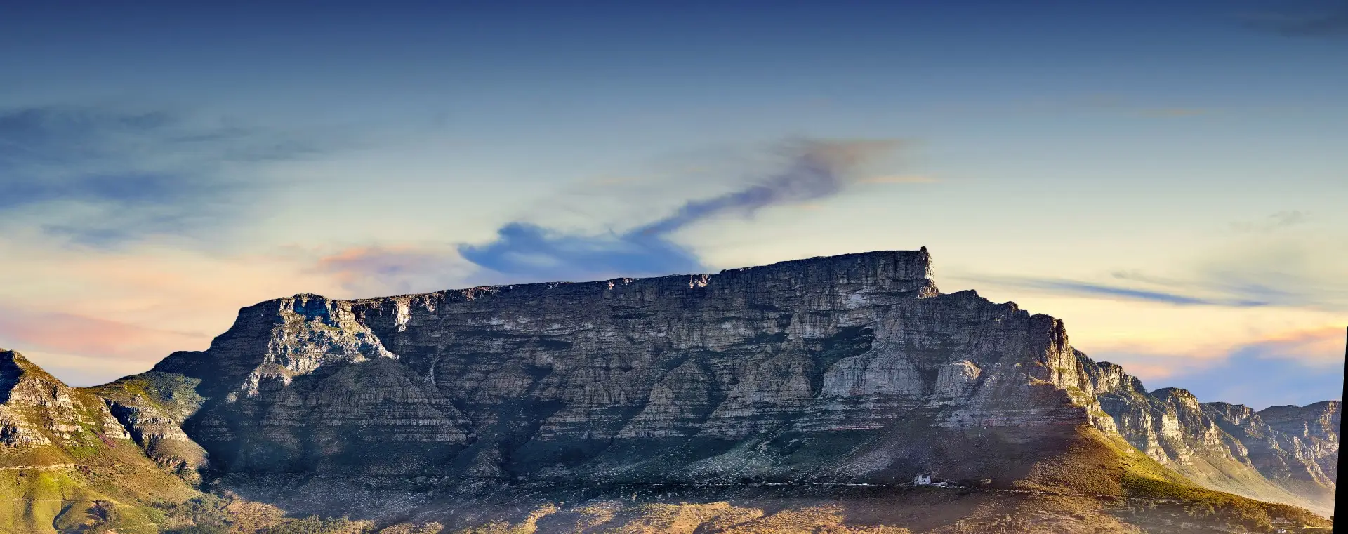 This eye-level shot reveals a majestic mountain range, showcasing rugged textures under a bright blue sky. Hues of green and brown color the slopes, while the mountain's steep sides create dramatic shadows. The scene is peaceful, highlighting the natural beauty of the area. This image can be used for travel advertisements, nature documentaries, and geographic studies focused on earth sciences.
